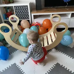 Roczne dziecko bawi się z kolorowymi balonami przy drewnianej kołysce. To idealne miejsce do rozwoju metodą Montessori.