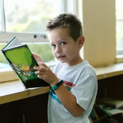 Chłopiec czyta książkę przy oknie, czując się samotny, bo dziecko boi się dzieci w przedszkolu.