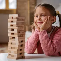 Uśmiechnięta dziewczynka zapatrzona w wieżę z klocków. To jedna z tych top zabawek, które zapewniają mnóstwo emocji.