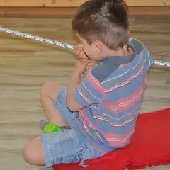 Chłopiec z obniżonym napięciem mięśniowym u 6 latka, siedzi na czerwonym kocu, bawi się zieloną zabawką.