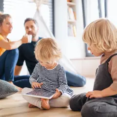 Dzieci pochłonięte tabletem, rodzice w tle. Czasem mówienie nie jest potrzebne, gdy technologia zajmuje uwagę.