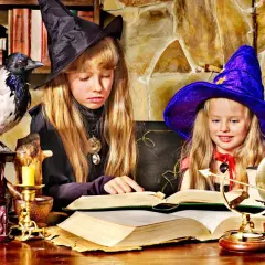Dwie dziewczynki w strojach czarownic tworzą magiczne prace plastyczne na Andrzejki, otoczone tajemniczymi rekwizytami.