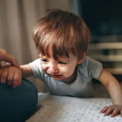 Małe dziecko płacze, gdy mama wychodzi. Trzyma się jej ręki, nie chcąc jej puścić.