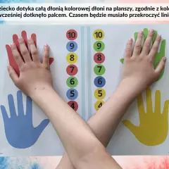 Dziecko dotyka dłonią kolorowych śladów na planszy, dopasowując je do cyfr. To ciekawe rysunki z kropek, które pomagają w nauce.