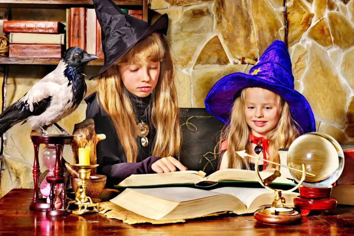 Dwie dziewczynki w strojach czarownic tworzą magiczne prace plastyczne na Andrzejki, otoczone tajemniczymi rekwizytami.