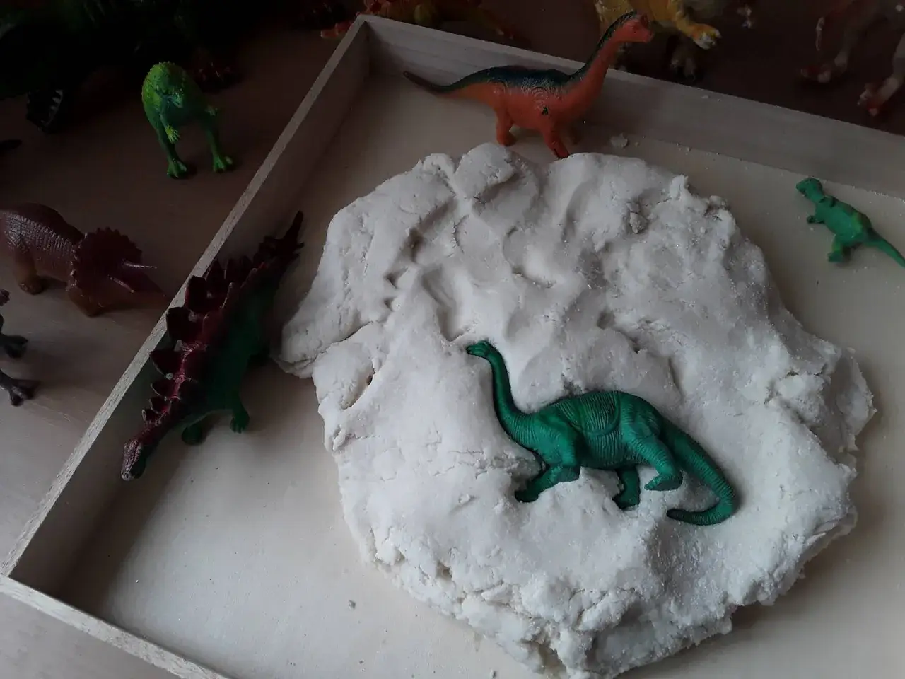 Zabawa w dzień dinozaura: figurki prehistorycznych gadów w piaskownicy z masą plastyczną.