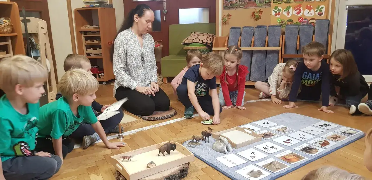Dzieci i nauczycielka bawią się figurkami zwierząt i kartami z tropami. Pedagogika zabawy w praktyce.