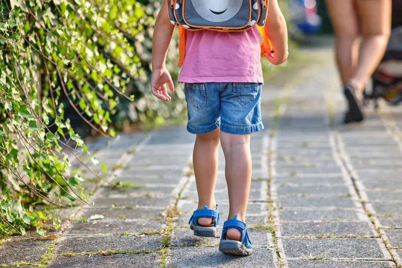 Dziecko w plecaku idzie ścieżką, symbolizując dojrzałość szkolną i nowy etap życia.