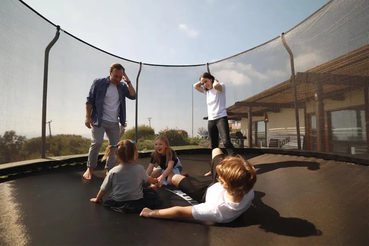 Rodzina cieszy się wspólnymi zabawami na trampolinie. Dzieci śmieją się, a rodzice patrzą z uśmiechem.