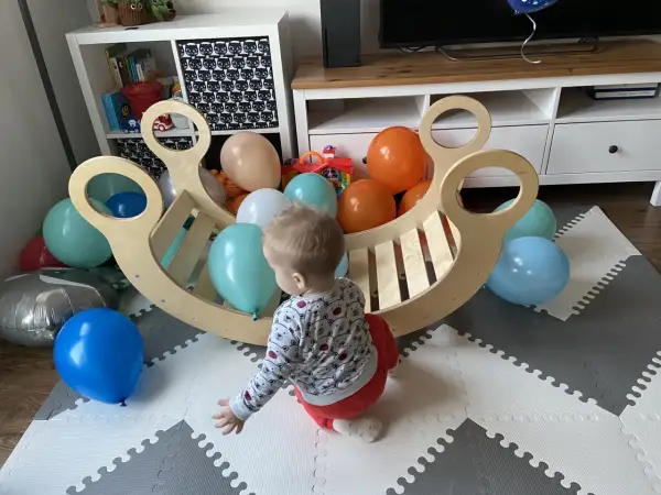 Roczne dziecko bawi się z kolorowymi balonami przy drewnianej kołysce. To idealne miejsce do rozwoju metodą Montessori.